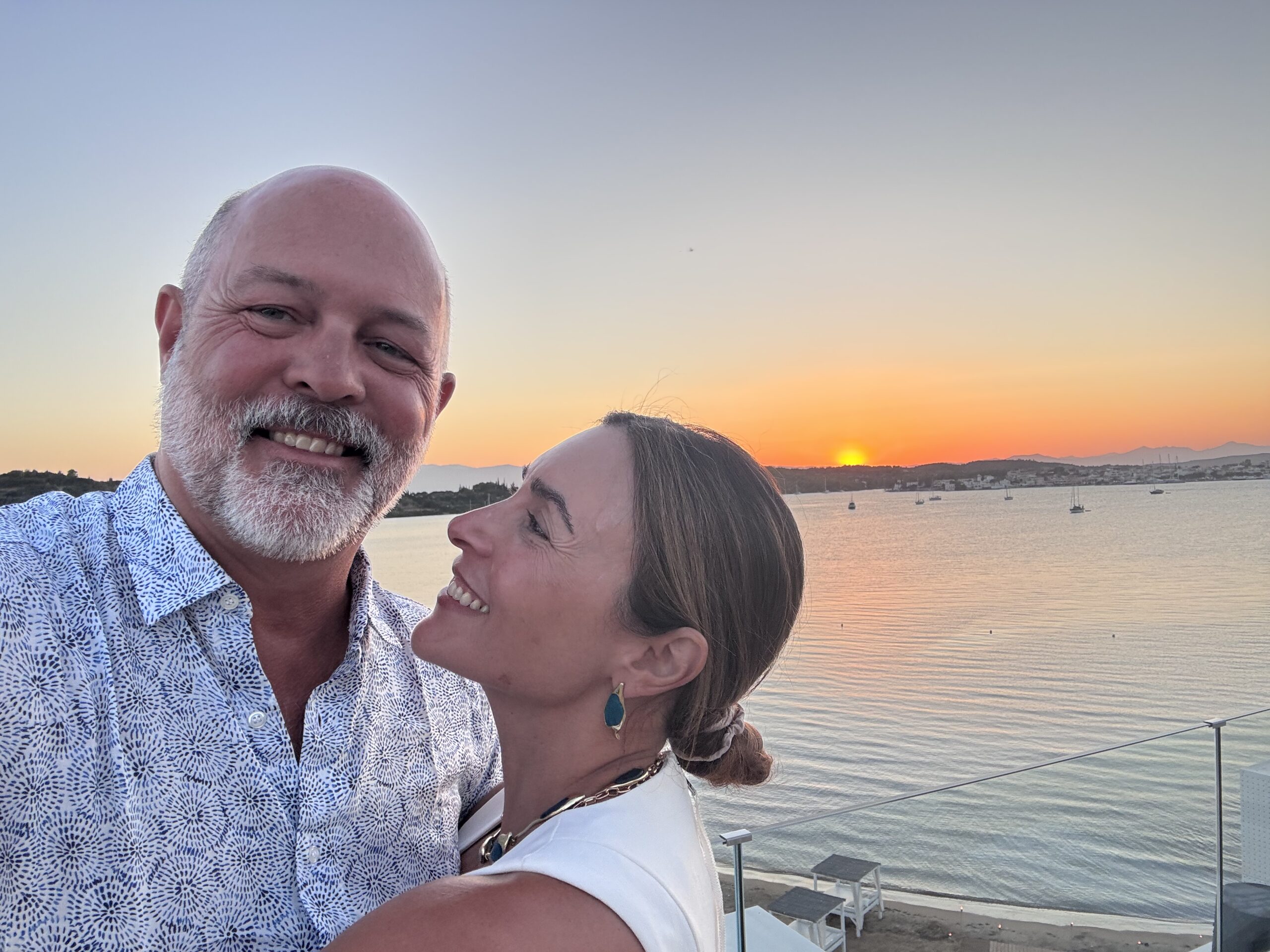 A woman gazing lovingly at her husband in front of a sunset on a cliff in Greece, symbolizing intimacy and connection in marriage.