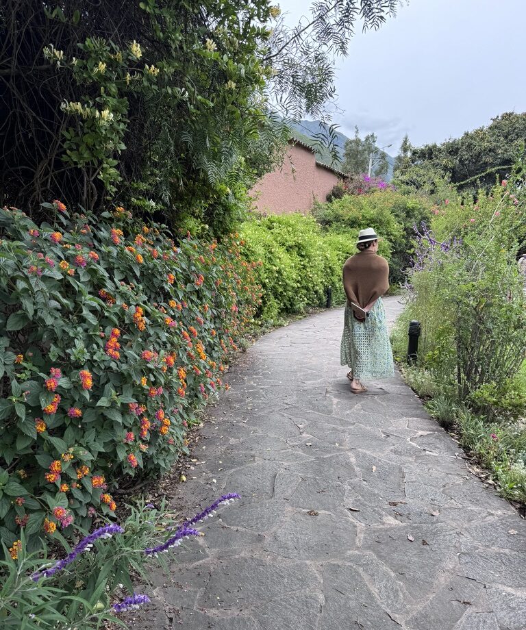 Danielle Alvarez Greer walks along a quiet stone path surrounded by lush greenery in the Sacred Valley of Peru.