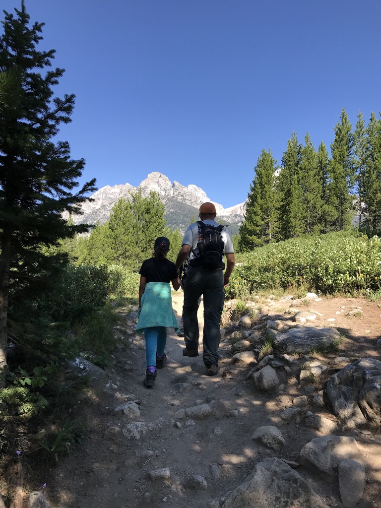 A father holding his daughter’s hand while hiking on a mountain trail in the Grand Tetons, illustrating trust, reassurance, and the safety of walking together when fear arises.