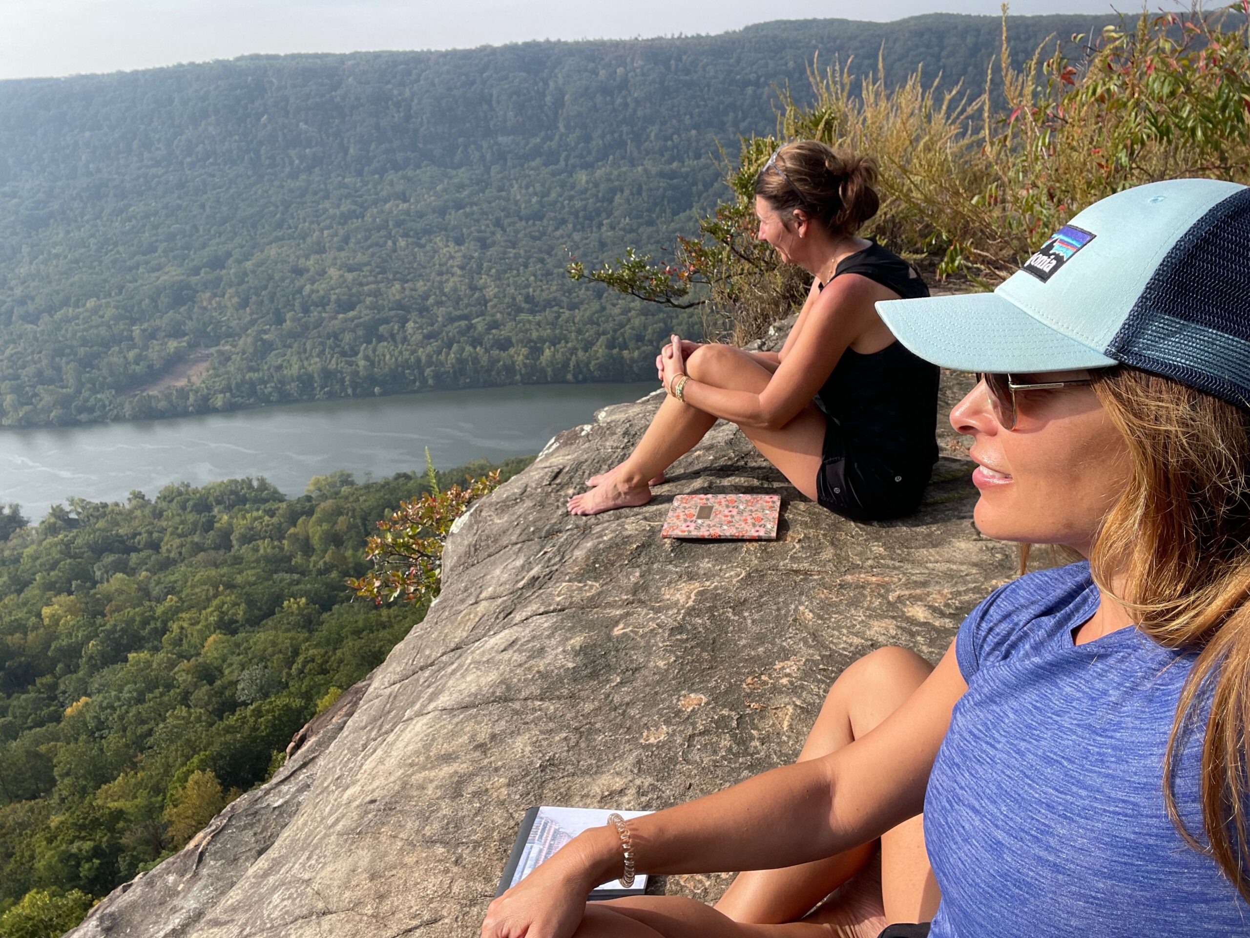 Christian women sitting on a mountain cliff overlooking a river, reflecting in nature during a season of emotional healing and identifying core beliefs behind reactions