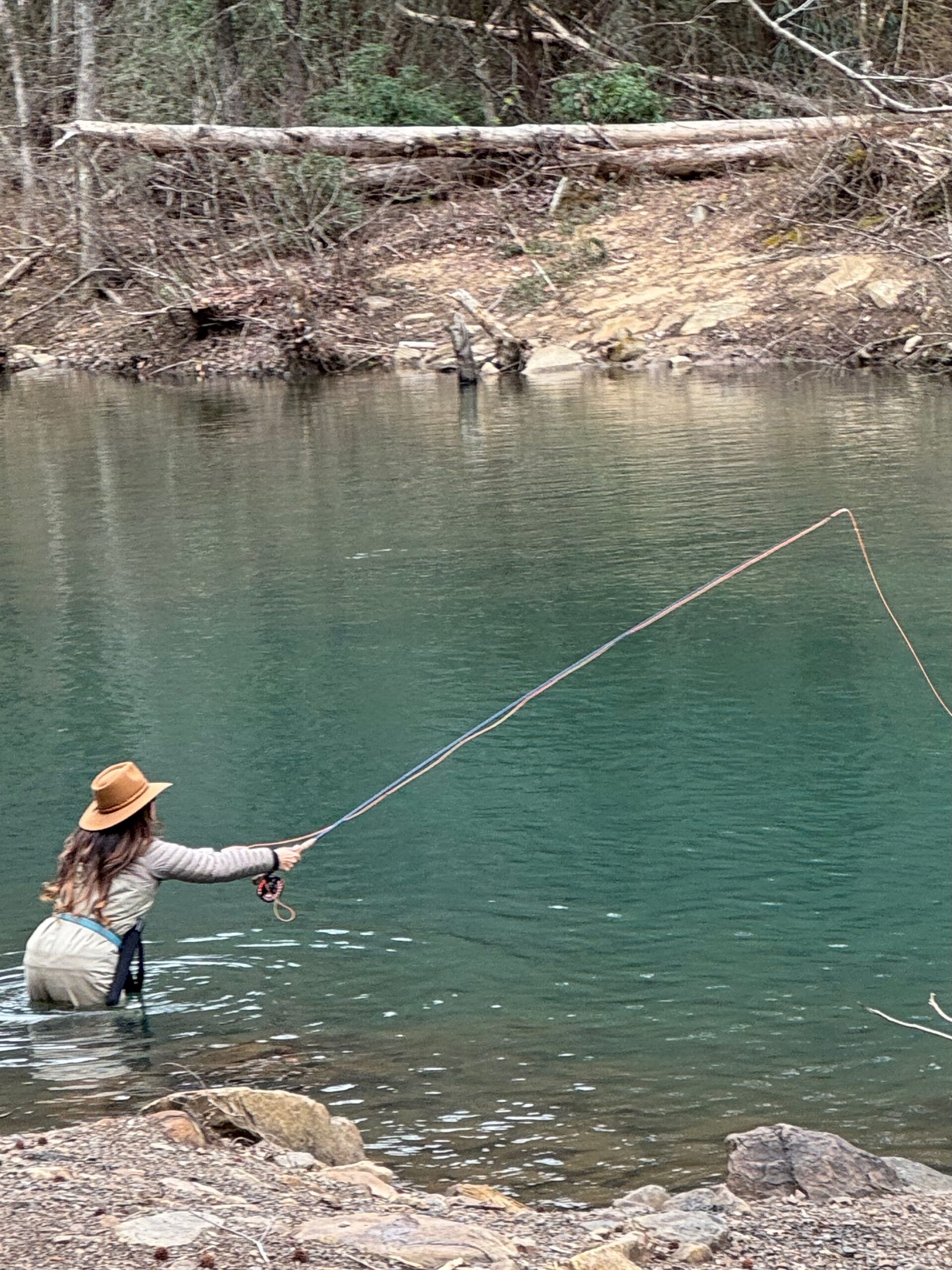 Woman fly fishing while standing in a calm river, surrounded by nature, reflecting a peaceful and present moment