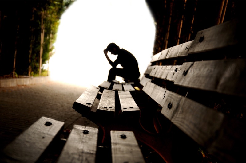 A silhouette of a person sitting alone on a bench with their head in their hands, symbolizing emotional exhaustion, grief, and seeking hope in darkness.
