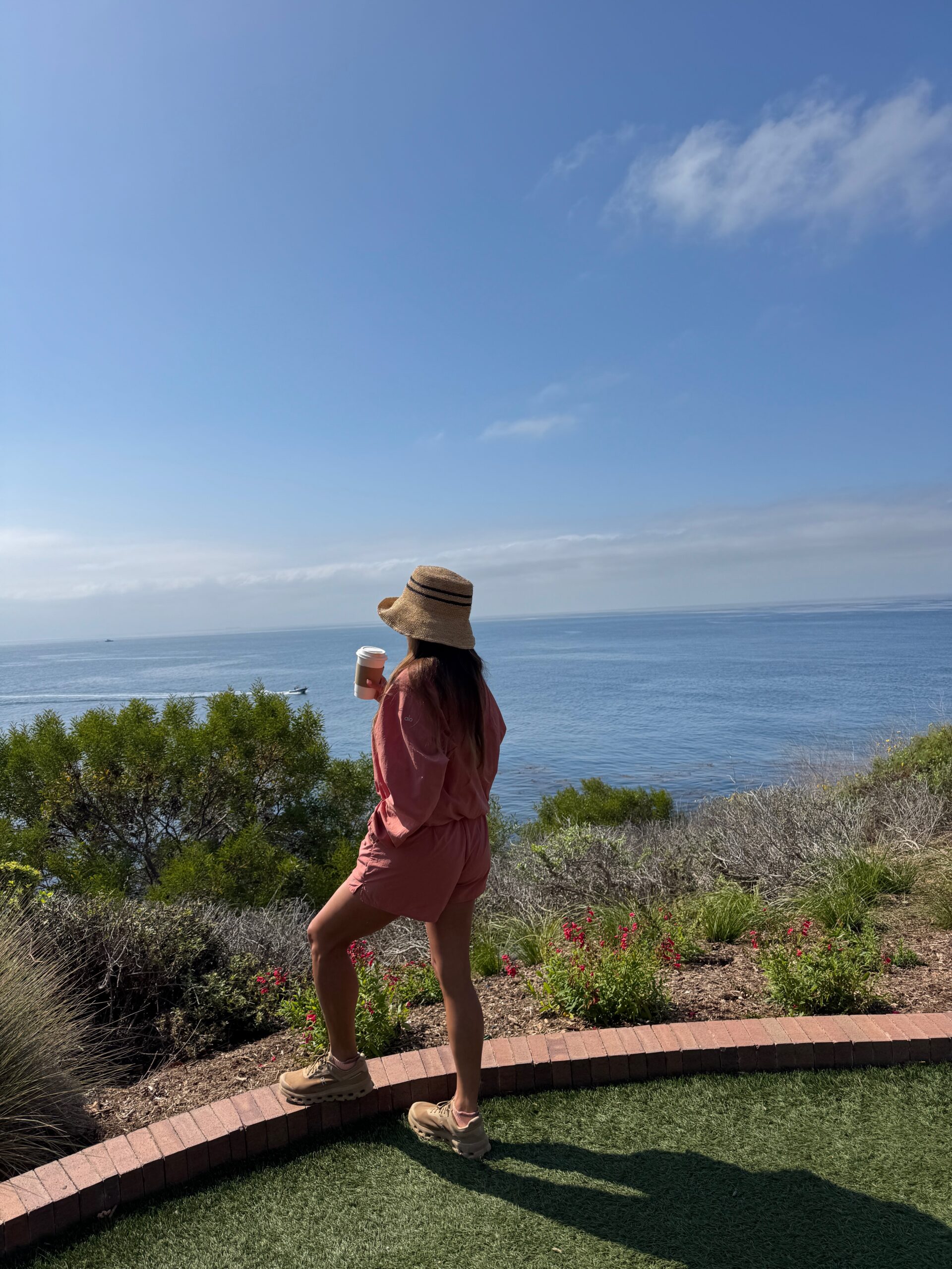 Woman standing with a cup of coffee and looking out over the ocean during a quiet moment of reflection.