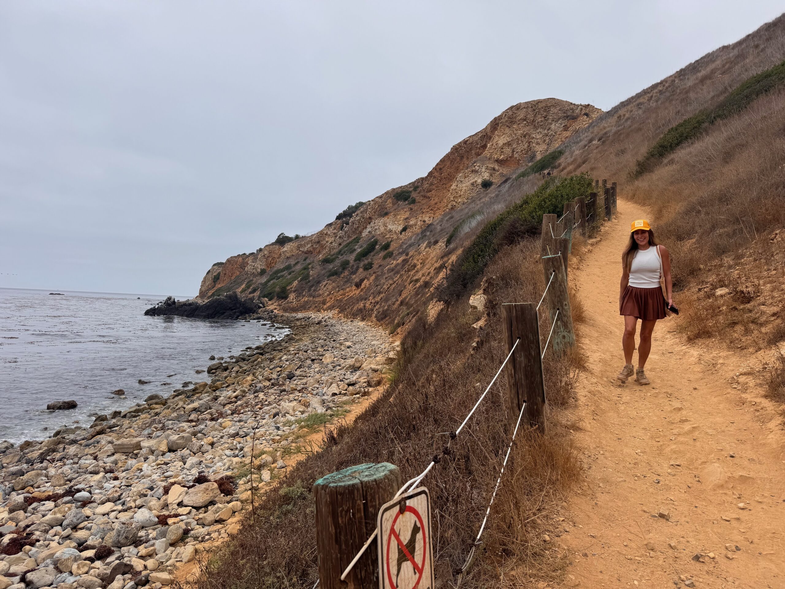 Woman walking along a coastal trail beside the ocean and cliffs, reflecting the journey of trusting God one faithful step at a time.