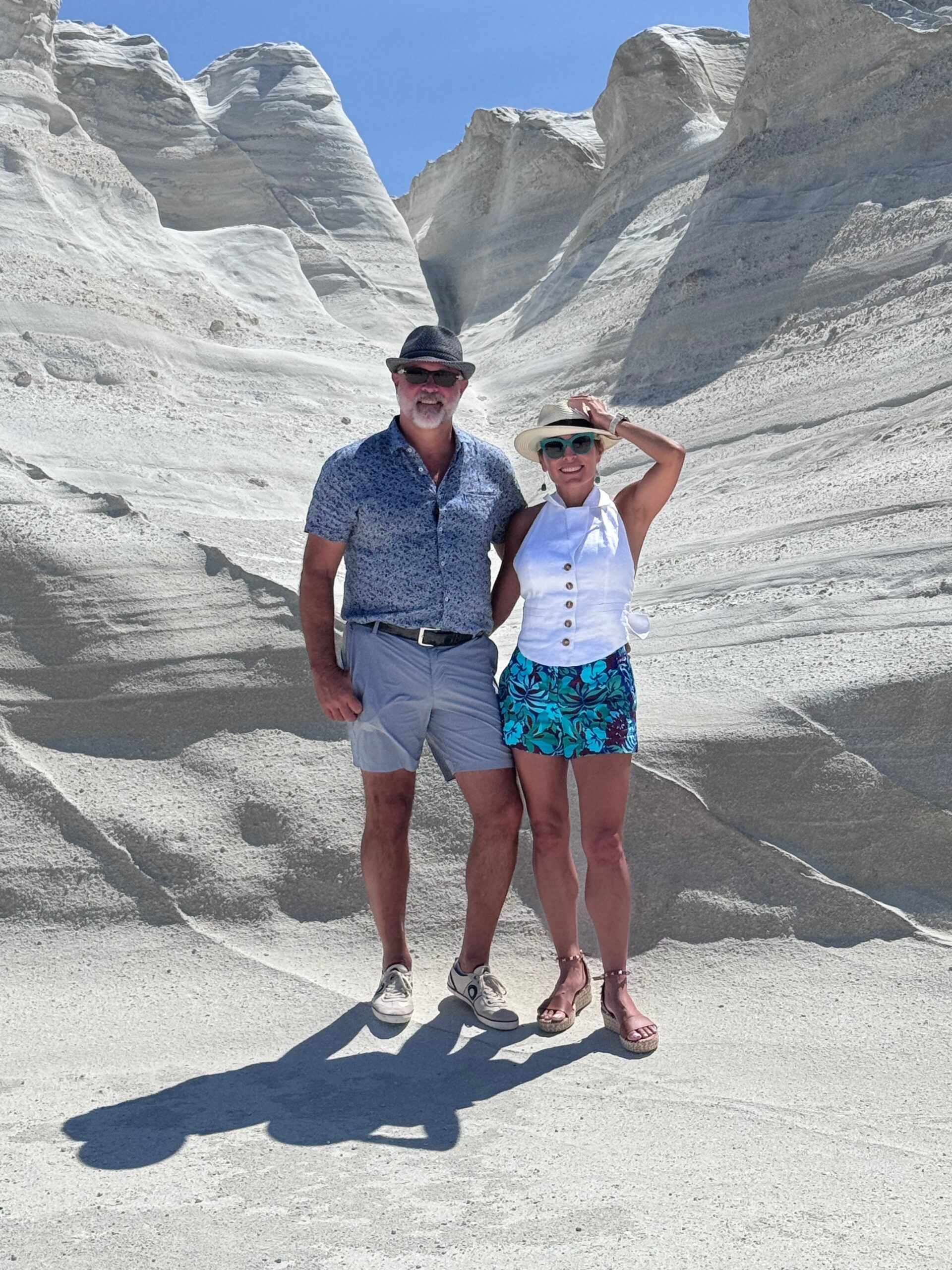 Danielle Alvarez Greer and her husband Jack standing together among the white rock formations of Milos, Greece, during a summer trip.